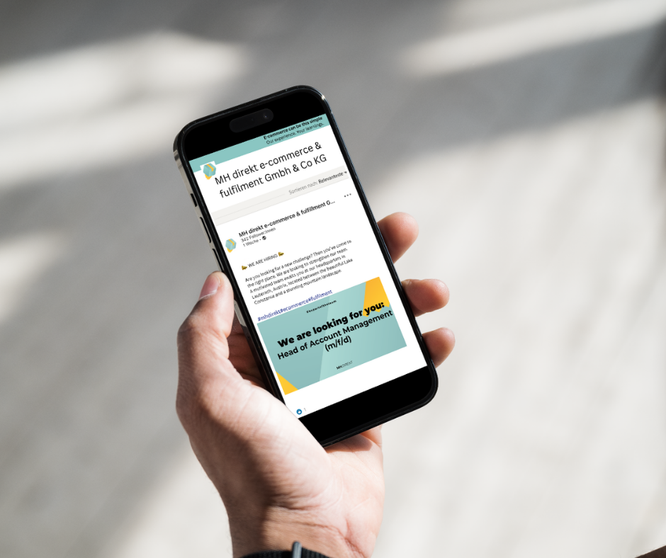 Person holding a smartphone displaying MH Direkt e-commerce and fulfilment recruitment post for Head of Account Management role